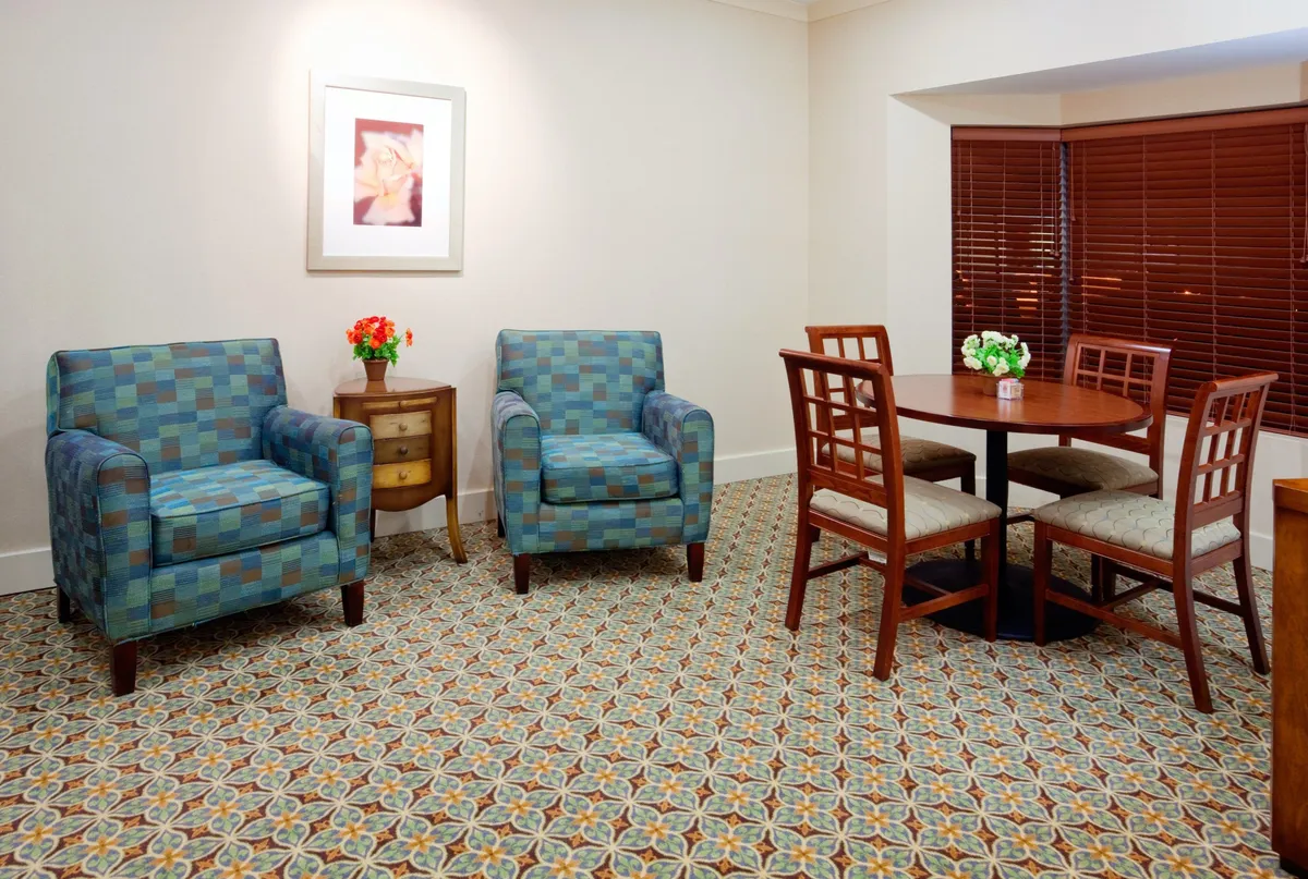 A cozy in-suite dining space with blue patterned chairs surrounding a wooden dining table topped with a floral centerpiece. The setting is perfect for enjoying home-cooked meals, casual conversations, or family gatherings in a welcoming, intimate environment.