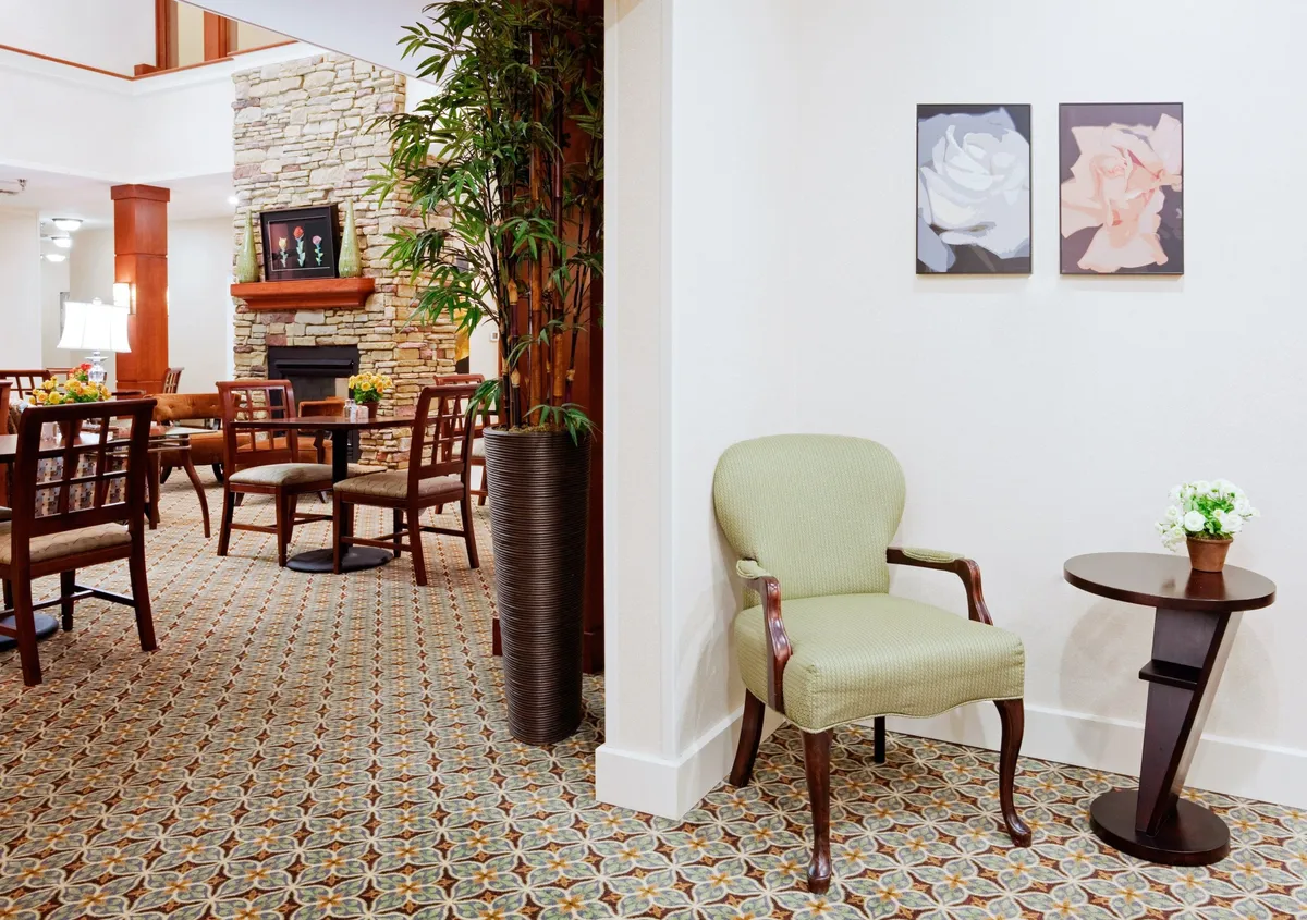 A peaceful corner with a green armchair, small side table, decorative plant, and a fireplace, complemented by artwork on the wall. The setting is calm and encourages moments of reading, reflection, or intimate conversation.