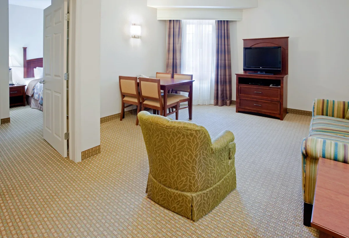 A welcoming living area with a comfy armchair, a dining table perfect for work or meals, and a television unit inviting guests to unwind and watch movies. The room feels cozy and versatile, with ample space for both relaxation and productivity.
