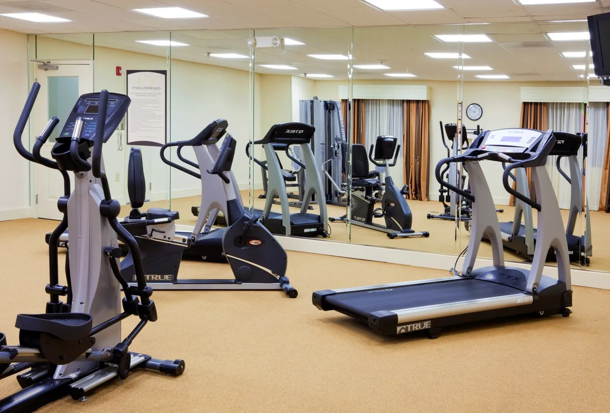 This image captures a modern fitness center featuring a treadmill, elliptical machine, and exercise bike in front of a mirrored wall. The space is bright and organized, with ample room for cardio and strength training routines.